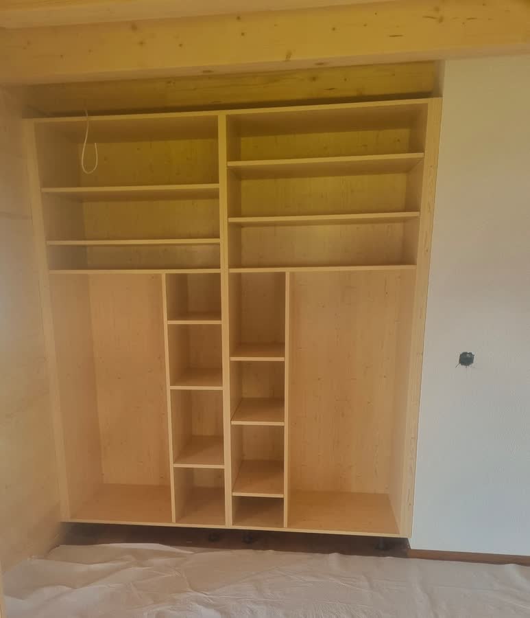 Dressing sur-mesure en bois clair encastré dans une niche, avec étagères hautes et colonnes de rangement.