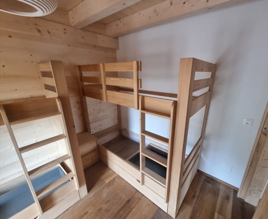 Deux ensembles de lits superposés en bois massif clair, avec échelles intégrées, garde-corps et tiroirs de rangement sous les couchages.