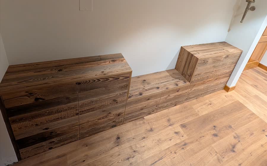 Meuble bas façon banquette réalisé en bois ancien, adossé à un mur.